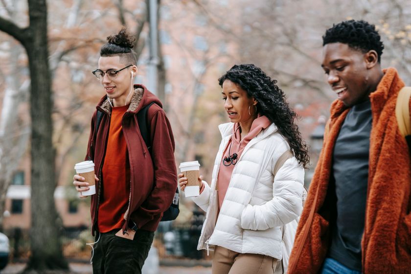 Three friends walking together, talking, coffee in hand