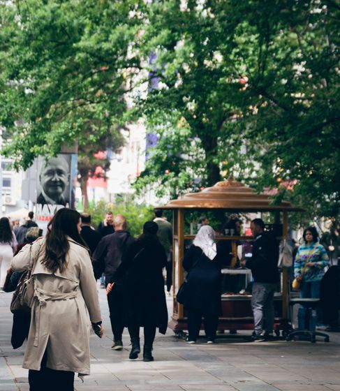 A tree-lined pedestrian street with people passing a market stall